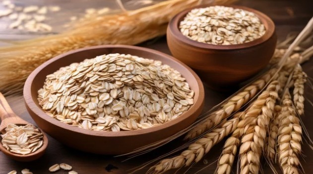 Two bowls of raw oats with oats plant stalks alongside them.